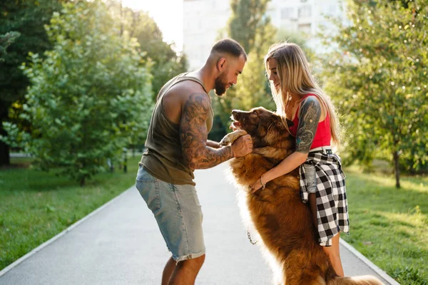 Joven pareja feliz jugando con su perro sonriendo en el parque — Foto de Stock