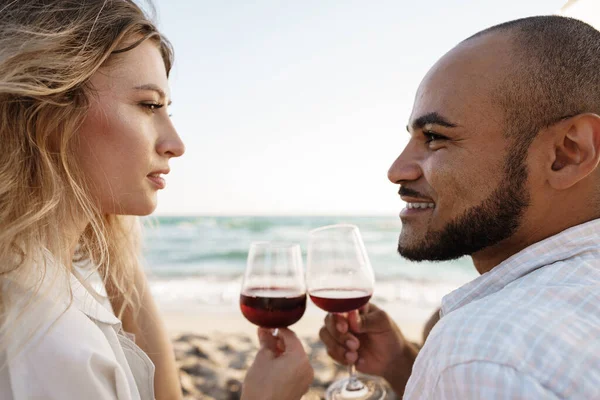 Retrato de una joven pareja sentada en la playa y bebiendo vino — Foto de Stock