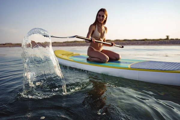 Close up of young woman sitting on a stand up paddle board — Stock Photo, Image