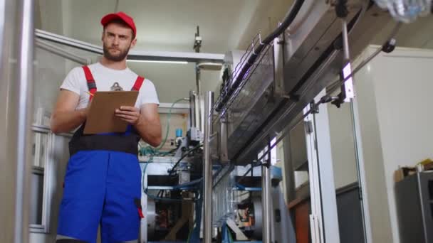Jonge fabrieksman in uniform maakt notities op klembord in waterfabriek — Stockvideo