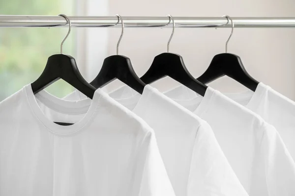 Reihe weißer T-Shirts auf Kleiderbügeln am Regal — Stockfoto
