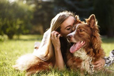Parkta köpeğini öpen genç kadının yakın portresi.