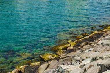 Sahildeki taşlara ve berrak suya yakın.