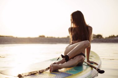 Seksi formda genç bir kadın. Denizde kürek tahtasında poz veriyor.