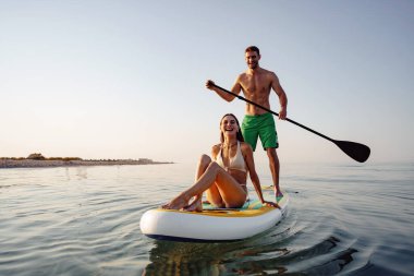Bir çift turist genç adam ve kadın denizde kürek çekerken eğleniyorlar.