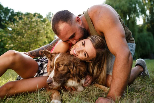 Young happy couple playing with their dog smiling in park — Stock Photo, Image