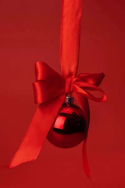 Schöne Christbaumkugel hängt auf rotem Satinband vor rotem Hintergrund — Stockfoto