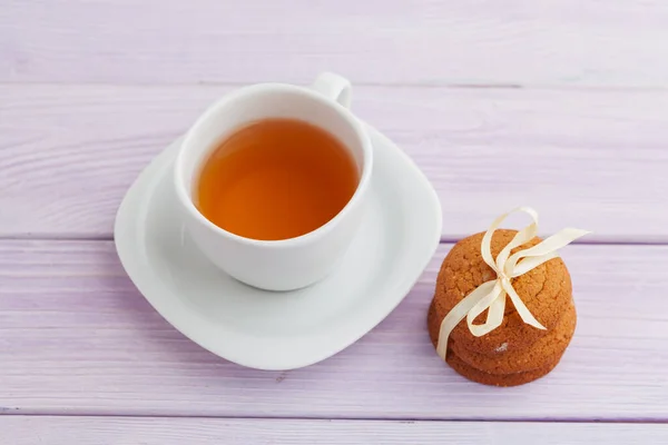 Чашка чая с печеньем на лиловом деревянном фоне — стоковое фото