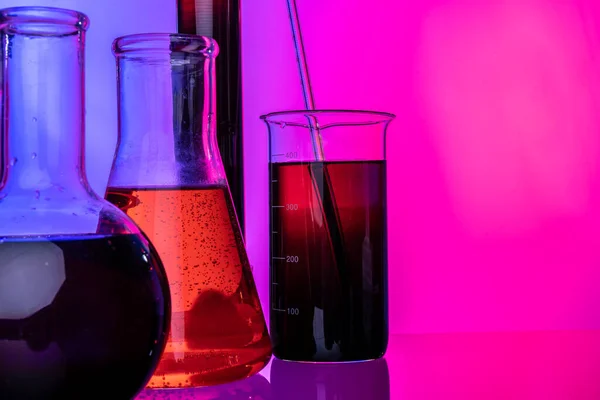 Tubos de vidrio de laboratorio con productos químicos sobre fondo rosa brillante —  Fotos de Stock