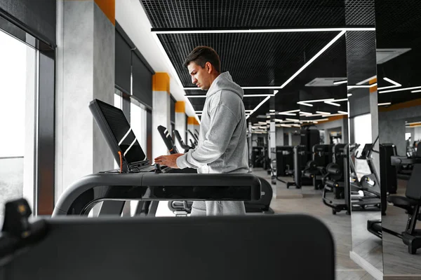 Portrét mladého muže v oranžové větrovce cvičení na fitness stroji v tělocvičně. — Stock fotografie