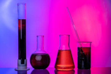 Parlak pembe arka planda kimyasallarla dolu laboratuvar cam tüpleri.