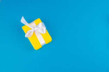 Mavi arka planda fiyonk ile süslenmiş hediye kutusunun düzlüğü