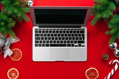 Kırmızı arka plan üst görünümünde kürk ağacı dalları ve noel süslemeleri ile Laptop
