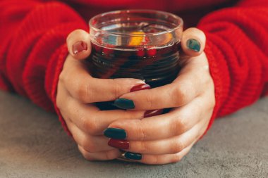 Elleri sıcak süveter giymiş kadınlar bir bardak sıcak şarap tutarlar.