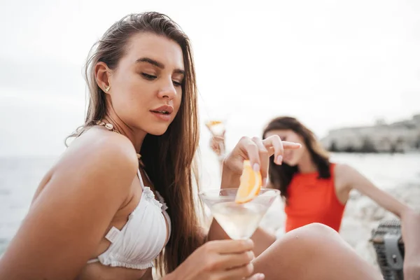 Twee jonge vriendinnen picknicken op het strand en drinken cocktails — Stockfoto