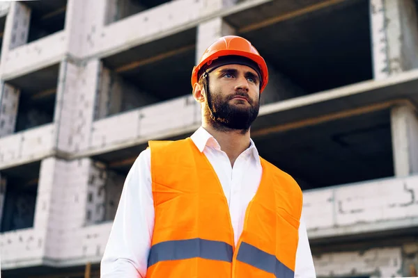 Byggare med hatt och skyddsväst stående på en kommersiell byggarbetsplats — Stockfoto