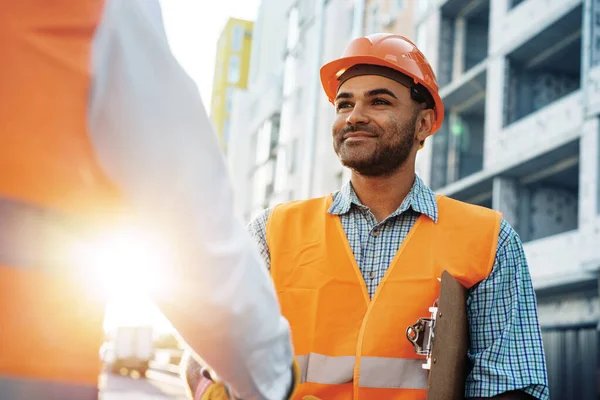 Dois homens engenheiros em roupas de trabalho apertando as mãos contra o canteiro de obras. — Fotografia de Stock