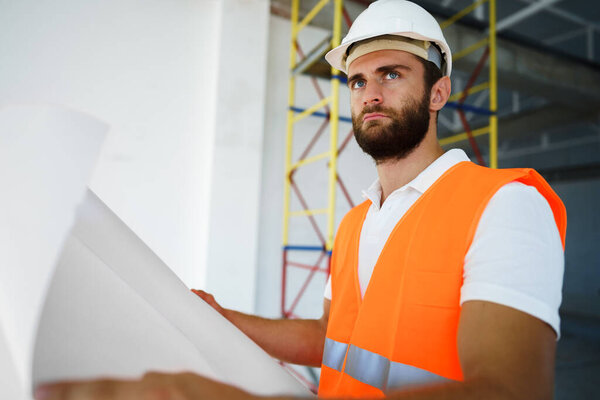 Builder or architect in hardhat supervising a project, looking at blueprints