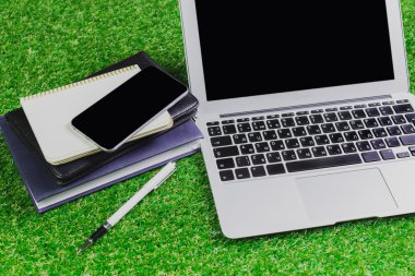 boş dizüstü bilgisayar, telefon, laptop ve kulaklık yeşil çimenlerin üzerinde