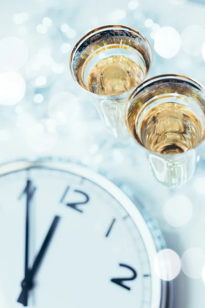 Foto vintage de copas con champán contra luces navideñas y reloj cerca de la medianoche — Foto de Stock