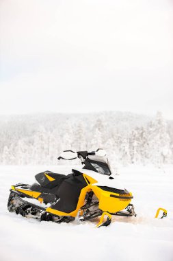 Sarı kar aracı kış manzarasının arka planında, karlı bir tarlada duruyor. Dikey çerçeve