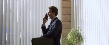 Ofisteki pencerenin önünde dikey perdelerin arkasında duran ve konuşmanın sonunda telefonla konuşan genç işadamı, arkasından gelen sürprizi öğreniyor..