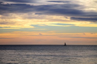 Güneş 'i kaplayan dramatik bulutlarla deniz manzarası ve günbatımının arka planında sakin bir deniz yüzeyi..