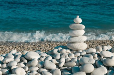 Tourette Rock Zen Piramidi taşların üzerinde beyaz çakıl taşı plajı mavi denizin arka planında.