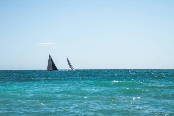 Yacht with black sail racing in the azure Mediterranean Sea.