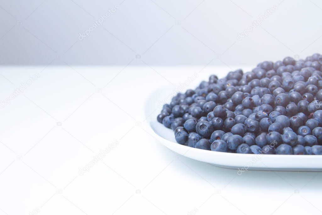 Part of a plate full of fresh blueberries on white background.
