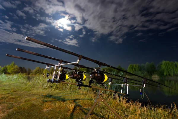 Carp spinning reel angling rods on pod standing. Night Fishing, Carp Rods, Cloudscape Full moon over lake.