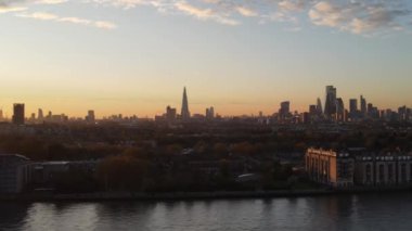 Arkaplanda günbatımında Londra 'nın merkez ufuk çizgisi ve çift ağaçlı Hilton otelinin hava taşımacılığı görüntüleri var. Thames Nehri üzerinde İHA Uçuşu.