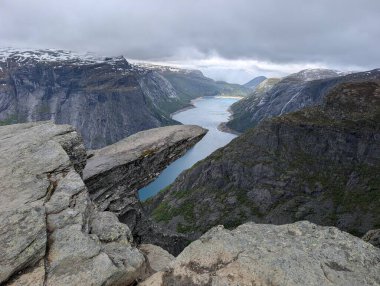 Meşhur Trolltunga kaya oluşumu derin mavi fiyortların üzerinde karamsar bulutlu bir gökyüzünün altında sarp kayalıklarla sarsılıyor..