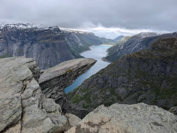 Meşhur Trolltunga kaya oluşumu derin mavi fiyortların üzerinde karamsar bulutlu bir gökyüzünün altında sarp kayalıklarla sarsılıyor..