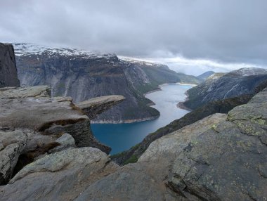 Meşhur Trolltunga kaya oluşumu derin mavi fiyortların üzerinde karamsar bulutlu bir gökyüzünün altında sarp kayalıklarla sarsılıyor..