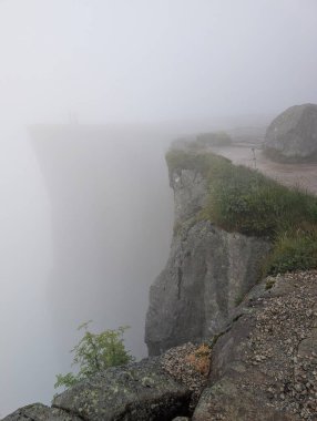 Büyük gri granit bir uçurum, çimenli bir kenarı ve kalın beyaz bir sisle örtülmüş büyük bir kaya parçası..