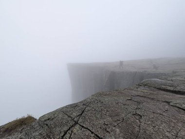 Yoğun siste bir dağın tepesinde bir insanın silueti..