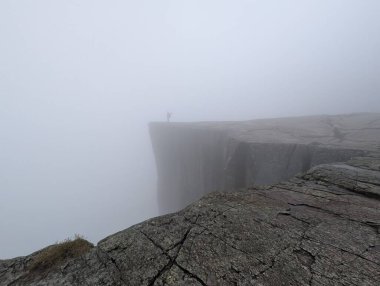 Düşük görüş mesafesi olan sisli bir uçurumun kenarında duran kişi..