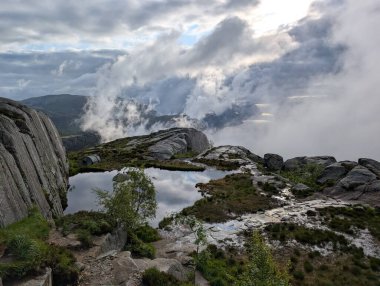 Yüksek açılı manzara, bulutlu bir gökyüzünü yansıtan küçük, sakin bir su havuzunu ortaya çıkarır..