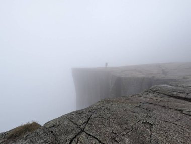 Düşük görüş mesafesi olan sisli bir uçurumun kenarında duran kişi..