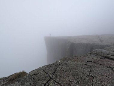 Yoğun siste bir dağın tepesinde bir insanın silueti..