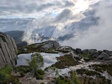 Yüksek açılı manzara, bulutlu bir gökyüzünü yansıtan küçük, sakin bir su havuzunu ortaya çıkarır..