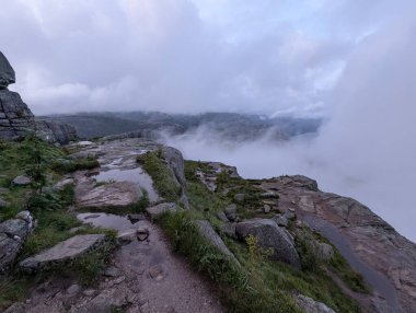 Kayalık arazi ve vadinin üzerindeki alçak bulutlarla puslu dağ manzarası.