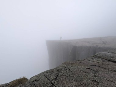 Düşük görüş mesafesi olan sisli bir uçurumun kenarında duran kişi..