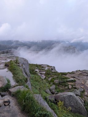 Vadinin üzerindeki kayalık uçurumlar ve bulutlarla puslu dağ manzarası.