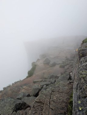 Büyük gri granit bir uçurum, çimenli bir kenarı ve kalın beyaz bir sisle örtülmüş büyük bir kaya parçası..