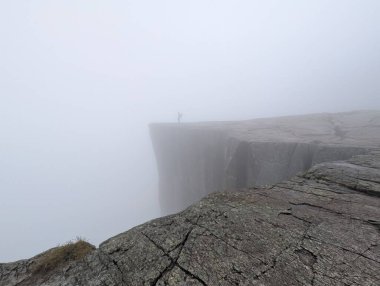 Düşük görüş mesafesi olan sisli bir uçurumun kenarında duran kişi..