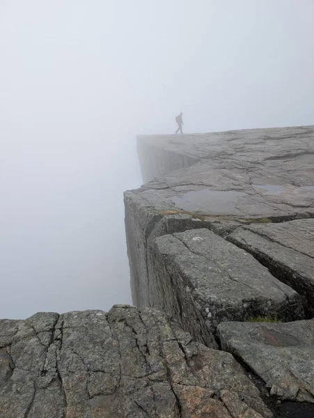 Düşük açılı görüş, geniş, çatlak granit bir platoya bakar. Yoğun beyaz bir sis tabakası içinde, kırmızı ceketli bir kişi uzaklarda yürür..