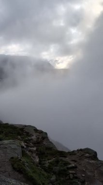 Gizemli, atmosferik bir manzara, derin bir dağ vadisini tamamen kaplayan yoğun, girdaplı beyaz sisi gösteriyor. Alt ön planda sadece küçük, kayalık bir çıkıntı görünüyor..