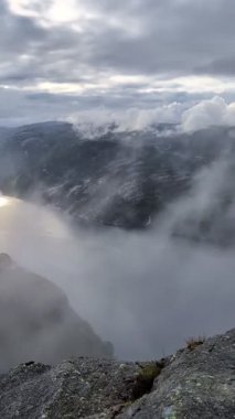 Kasvetli, bulutlu bir gökyüzü kalın, gri bulutlarla doludur. Bu bulutlar güneşi kısmen karartır. Kayalık bir dağın tepesinde yumuşak ve dağınık bir ışık yaratır..